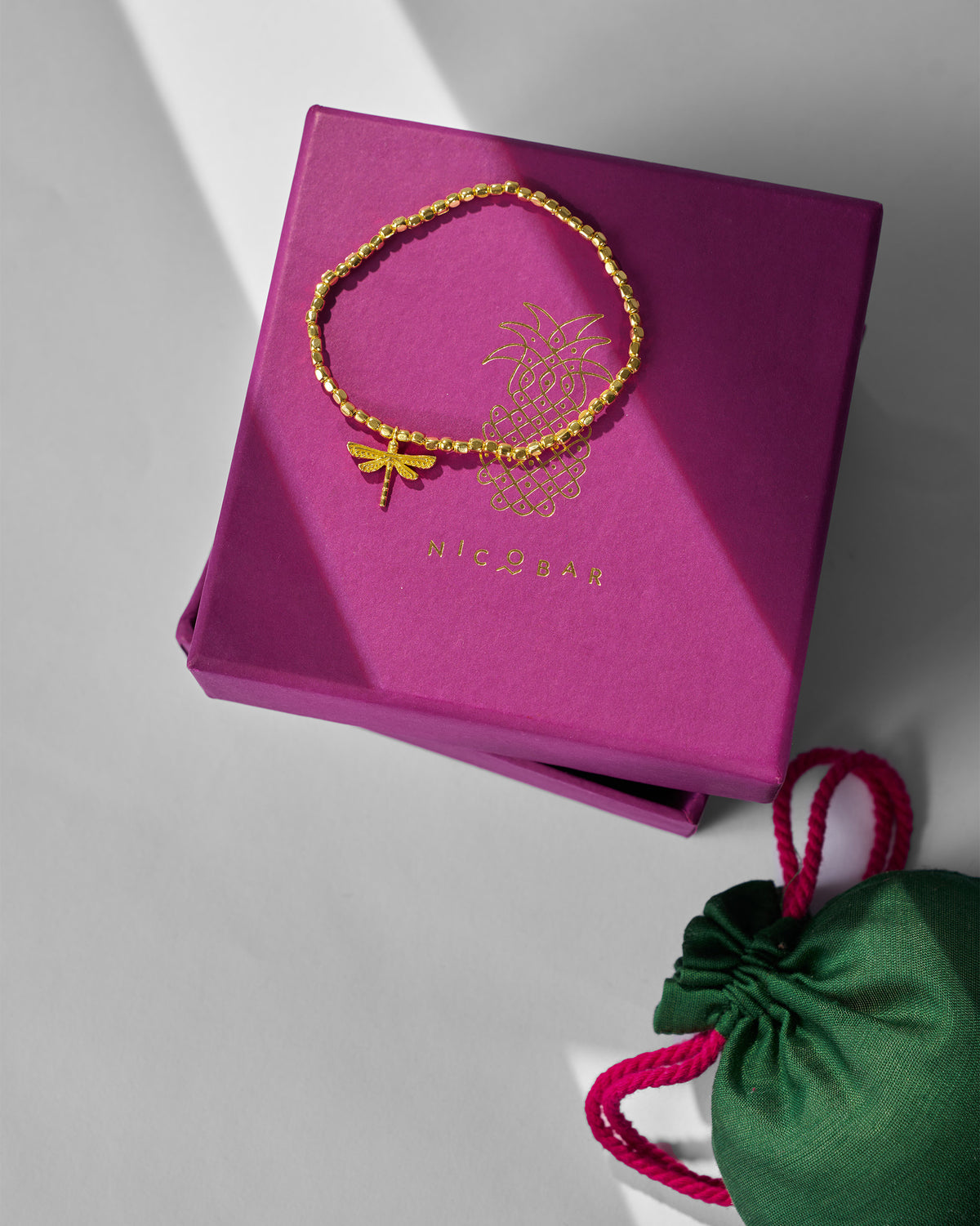 Dragonfly Bracelet resting on a magenta gift box beside a green pouch.