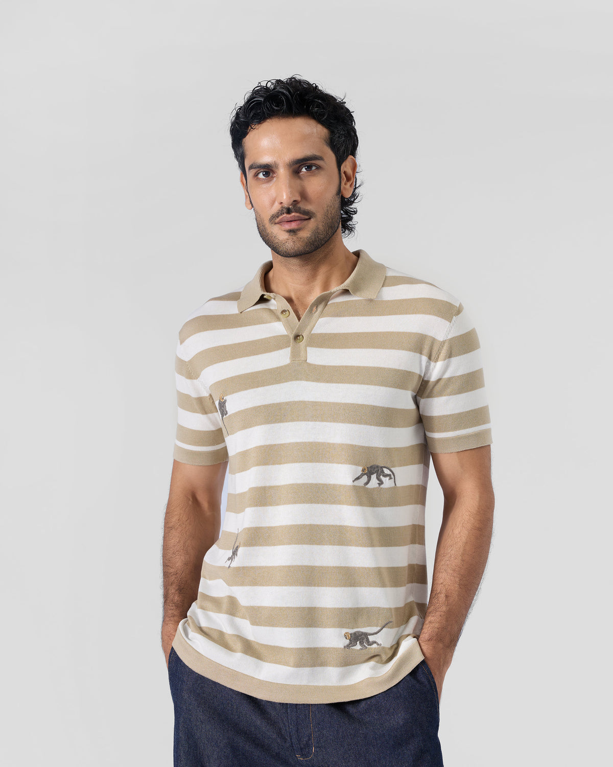 Person wearing an ivory and sand striped Macaque Polo with embroidered monkeys.