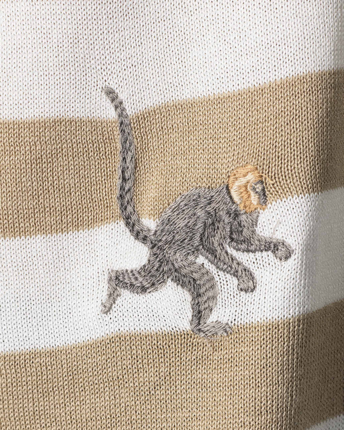 Close-up of an embroidered monkey on an ivory and sand striped Macaque Polo.