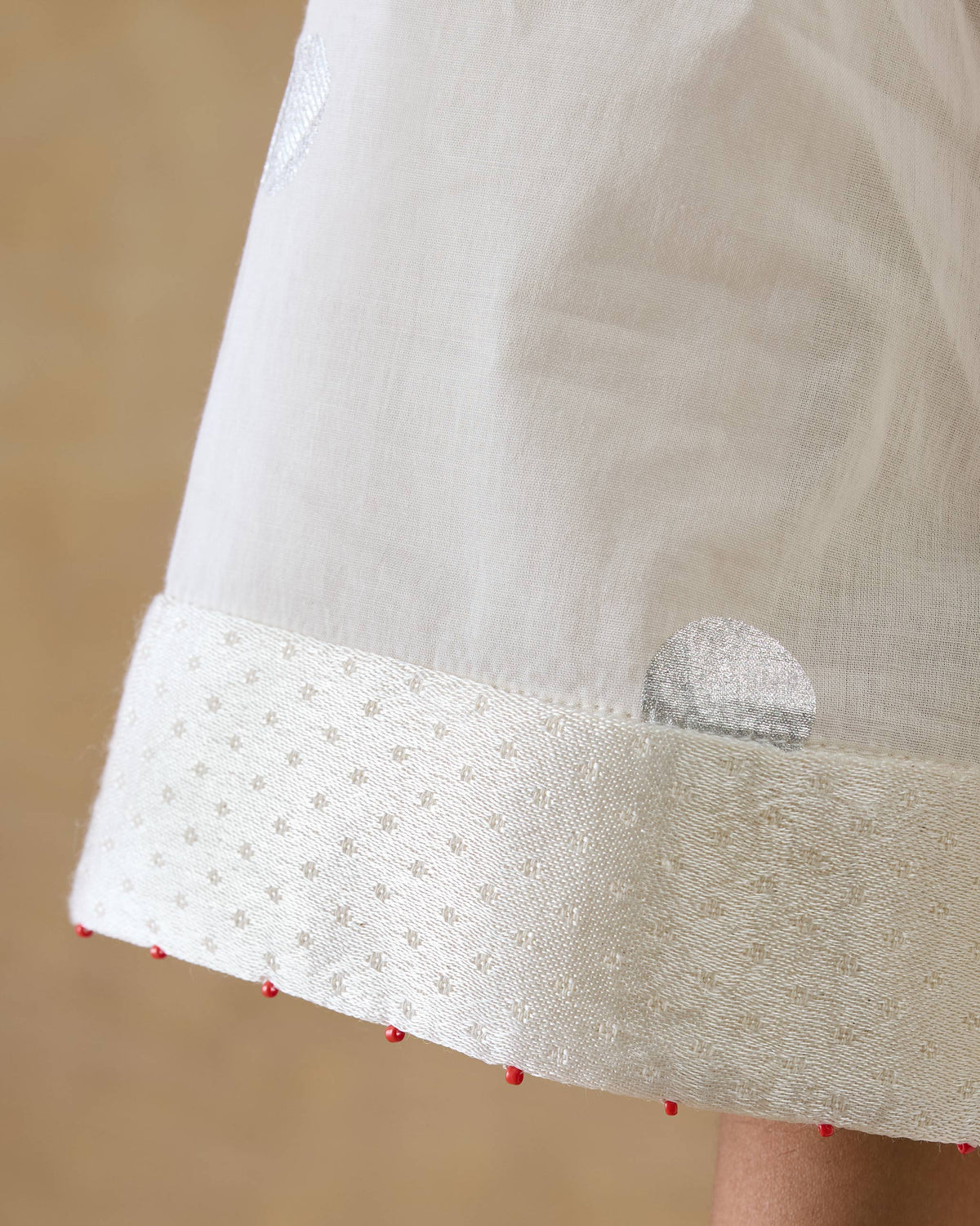 Close-up of a Rejoice kurta cuff with red bead trim.