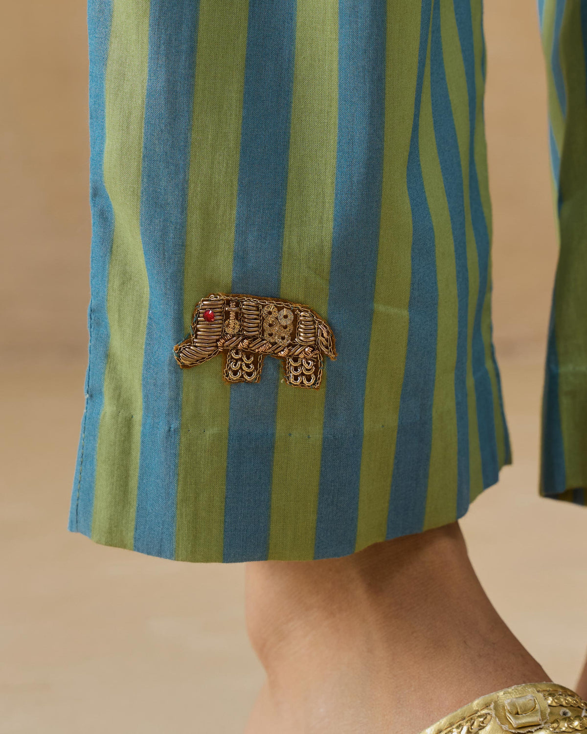 Close-up of a gold elephant embroidery on aqua and green striped Arzoie pants.