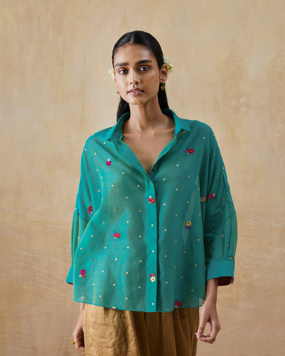 Person wearing an aqua Boxy shirt with floral embroidery and gold dots.