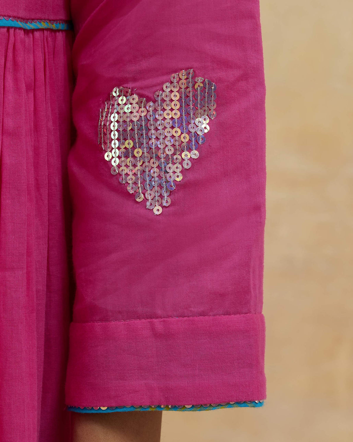 Close-up of a silver sequin heart on a bright pink Pintuck kurta sleeve.