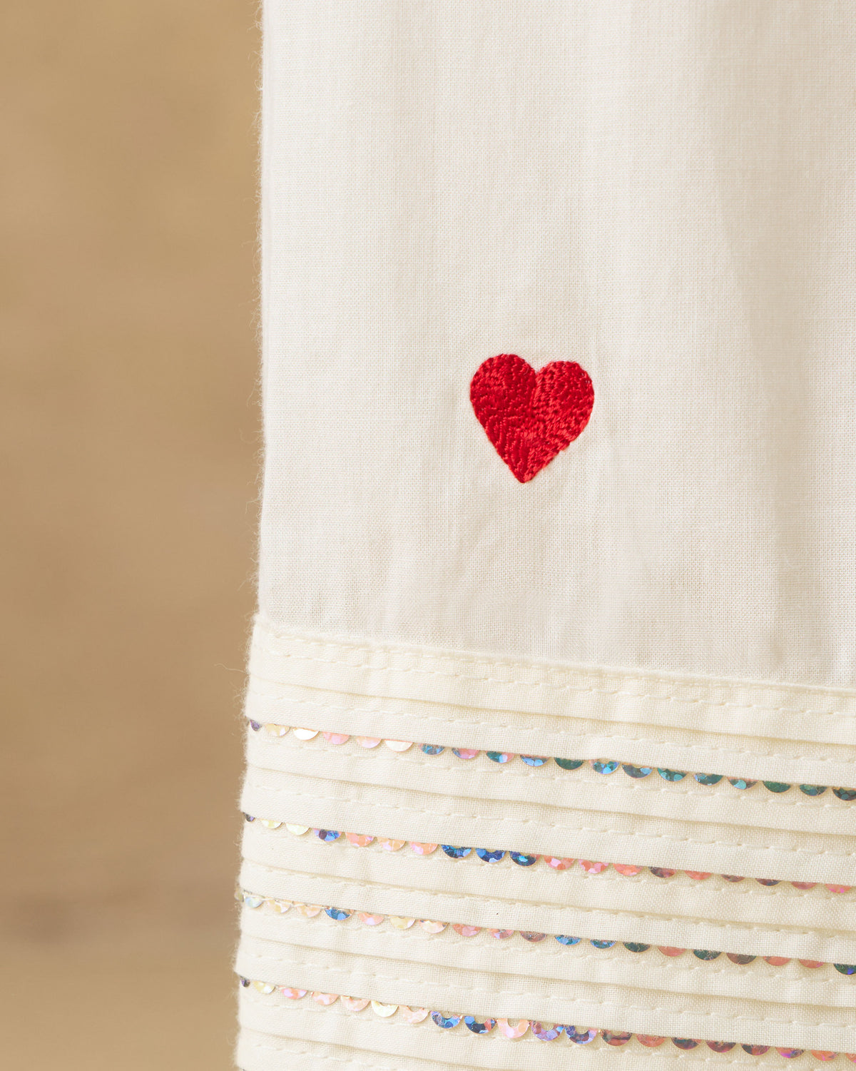 Close-up of a red heart and sequin pintucks on ivory Numa Pants.