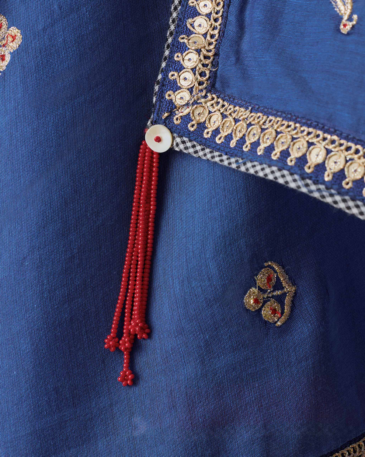 Close-up of a Leher dupatta border with gold embroidery and a red beaded tassel.