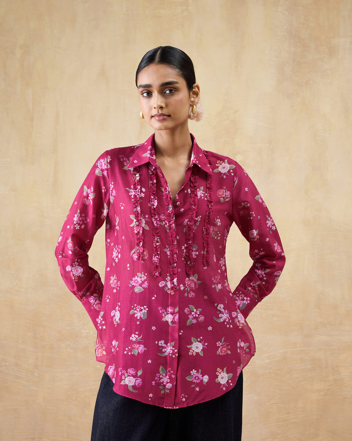 Person wearing a berry floral Kaveri shirt with ruffles along the button placket.