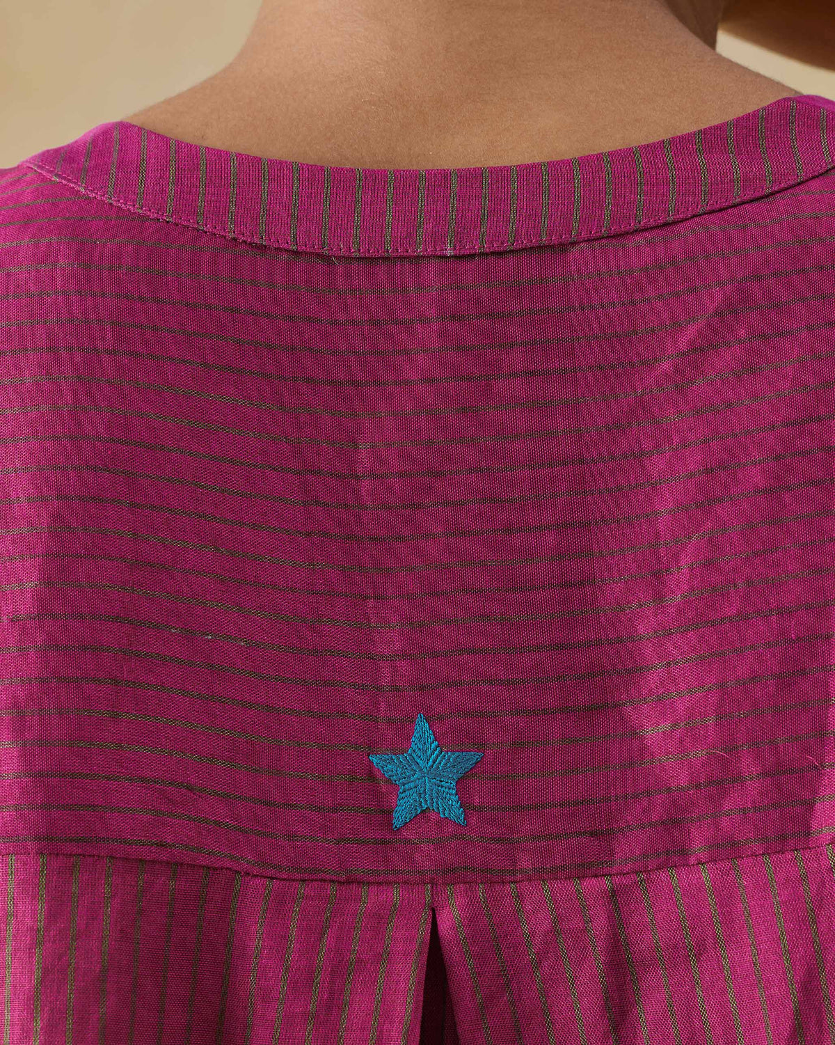 Close-up of a teal embroidered star on fuchsia striped Lazy Sunday tunic fabric.