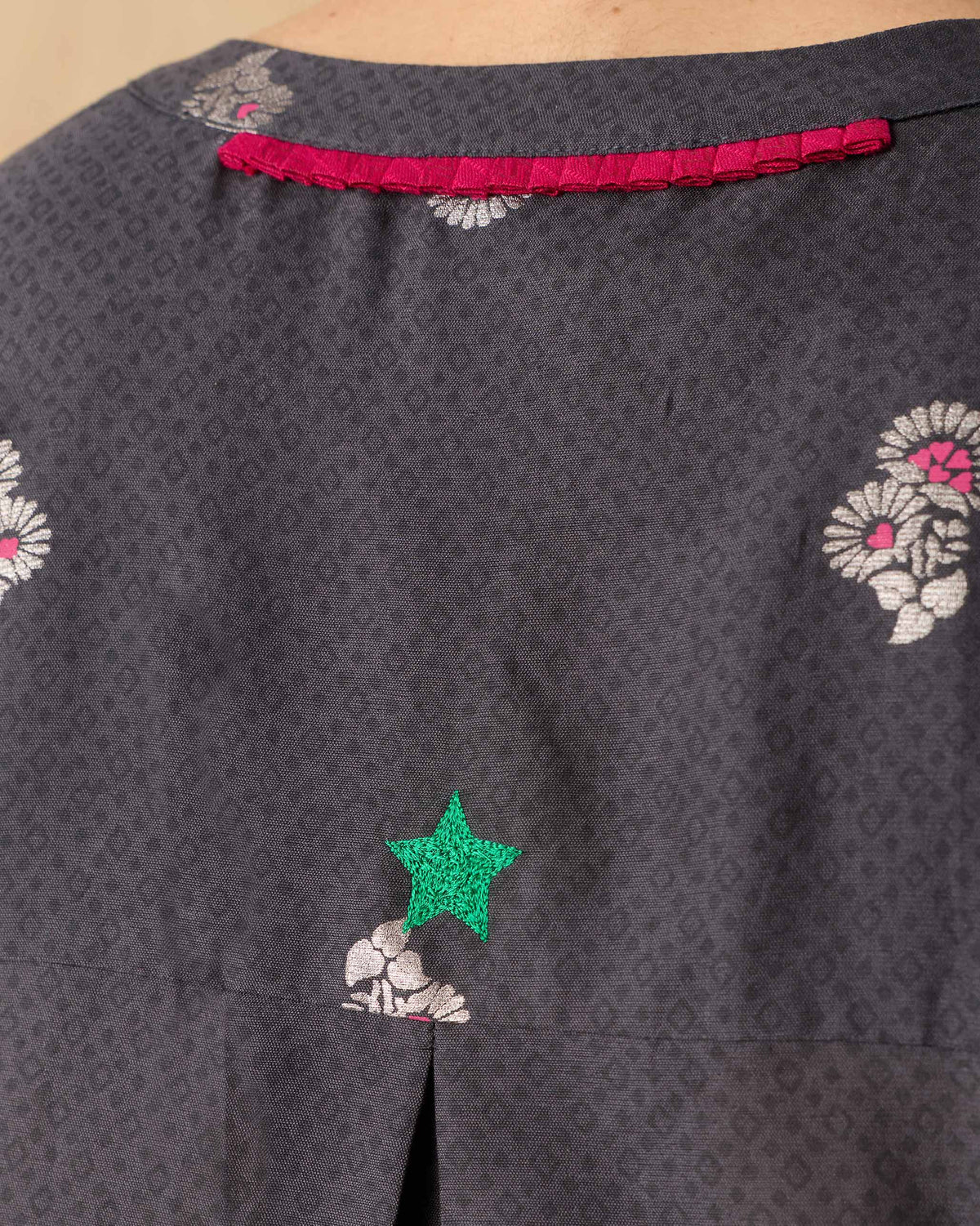 Close-up of magenta yoke trim and a green star on a charcoal Lazy Sunday tunic.