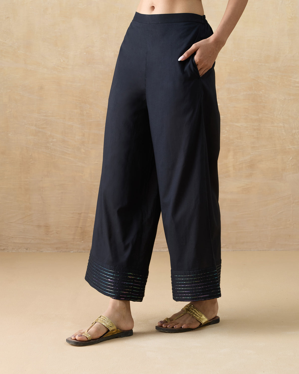 Black A-line pants with a hand in the side pocket and sequin hem.