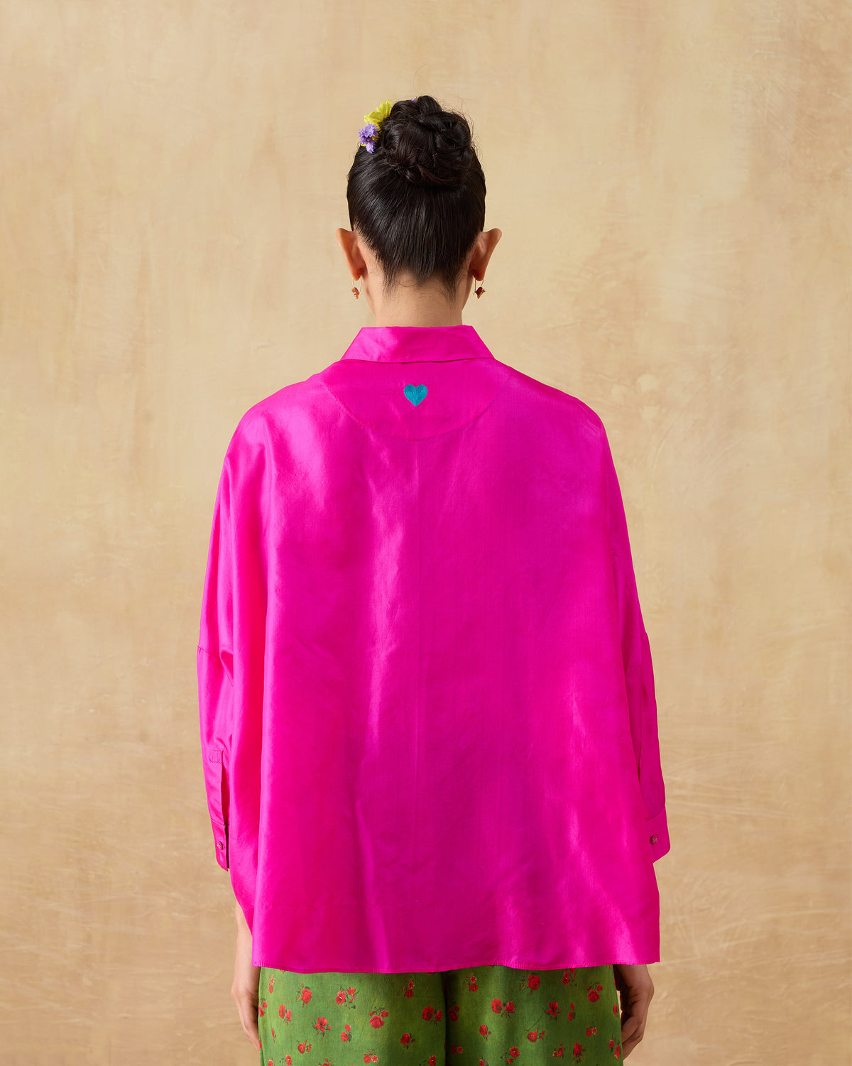 Back of a fuchsia pink silk boxy shirt with a teal embroidered heart below the collar.