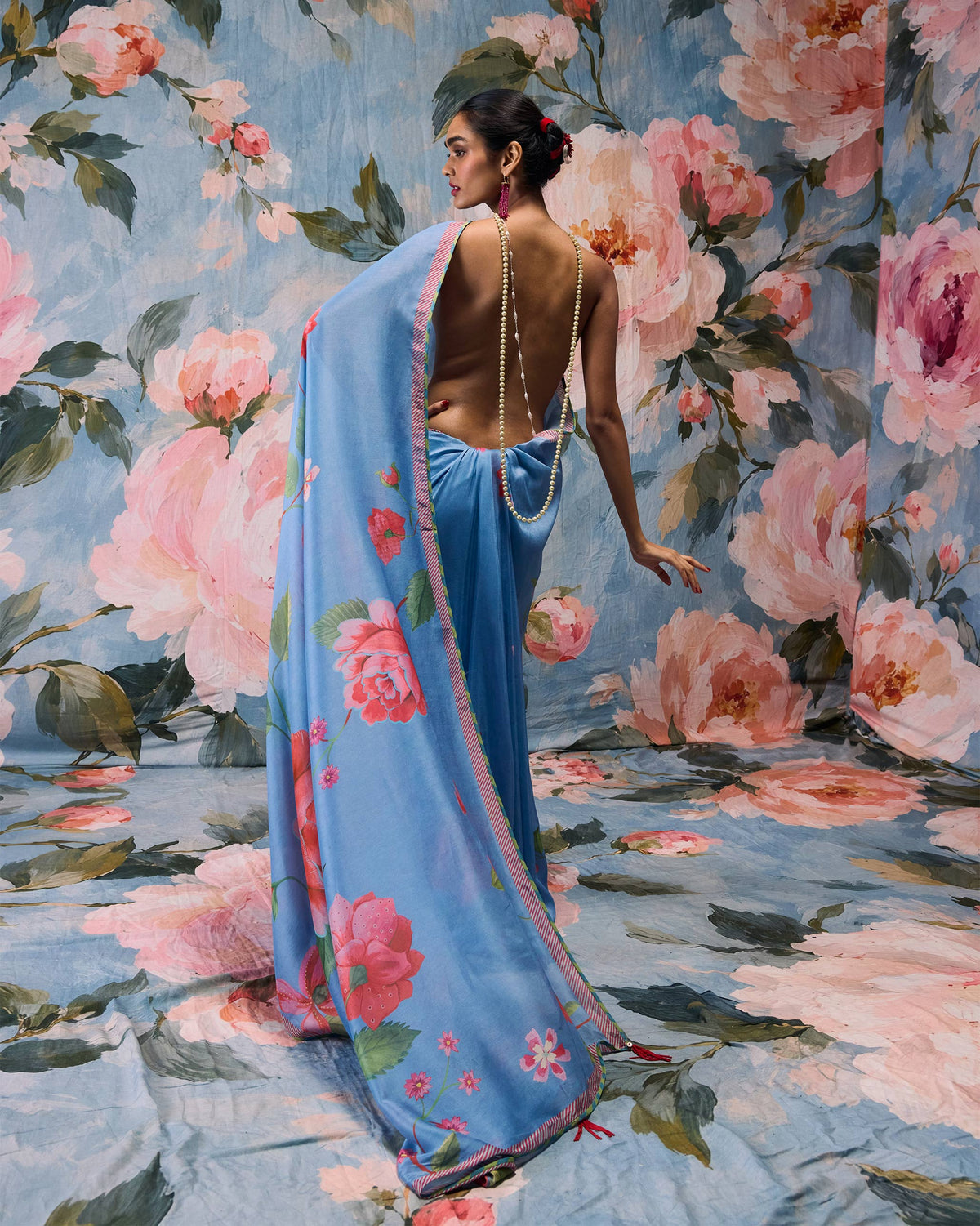 Back of a blue First Bloom sari with a pink rose print worn by a person.