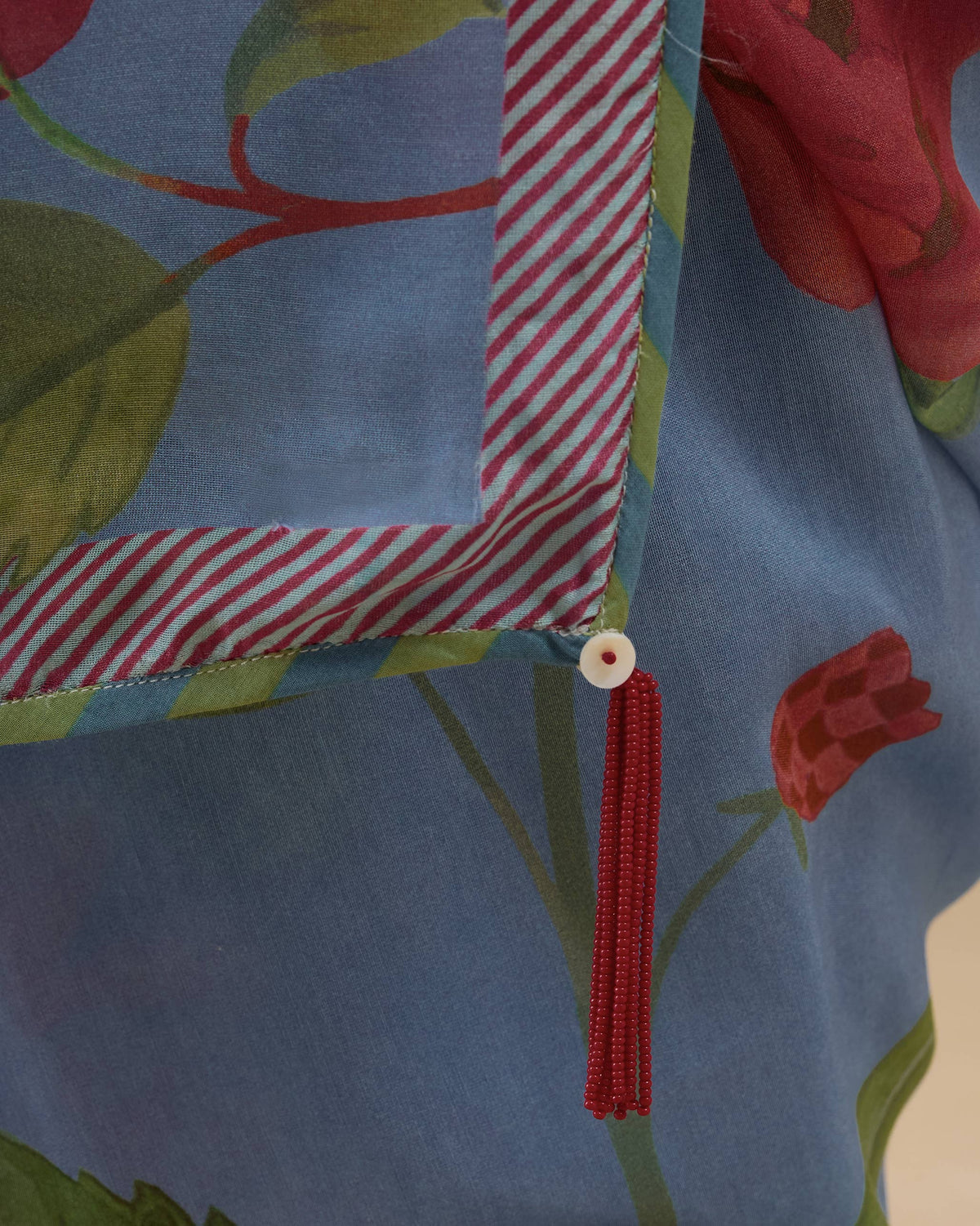 Close-up of a blue First Bloom sari showing a pink striped border and a red tassel.
