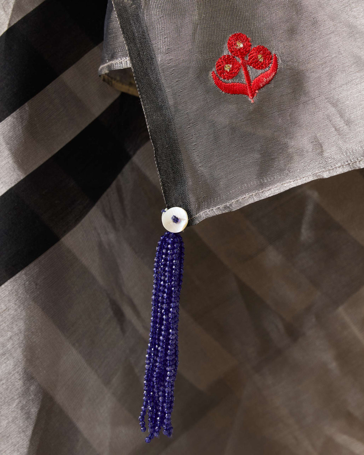 Close-up of a blue beaded tassel and red motif on a silver Party Stripes sari.
