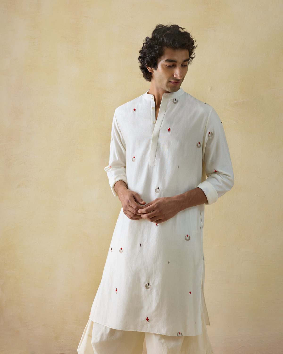 Person wearing an ivory Neckband Kurta with rolled sleeves and scattered embroidery.