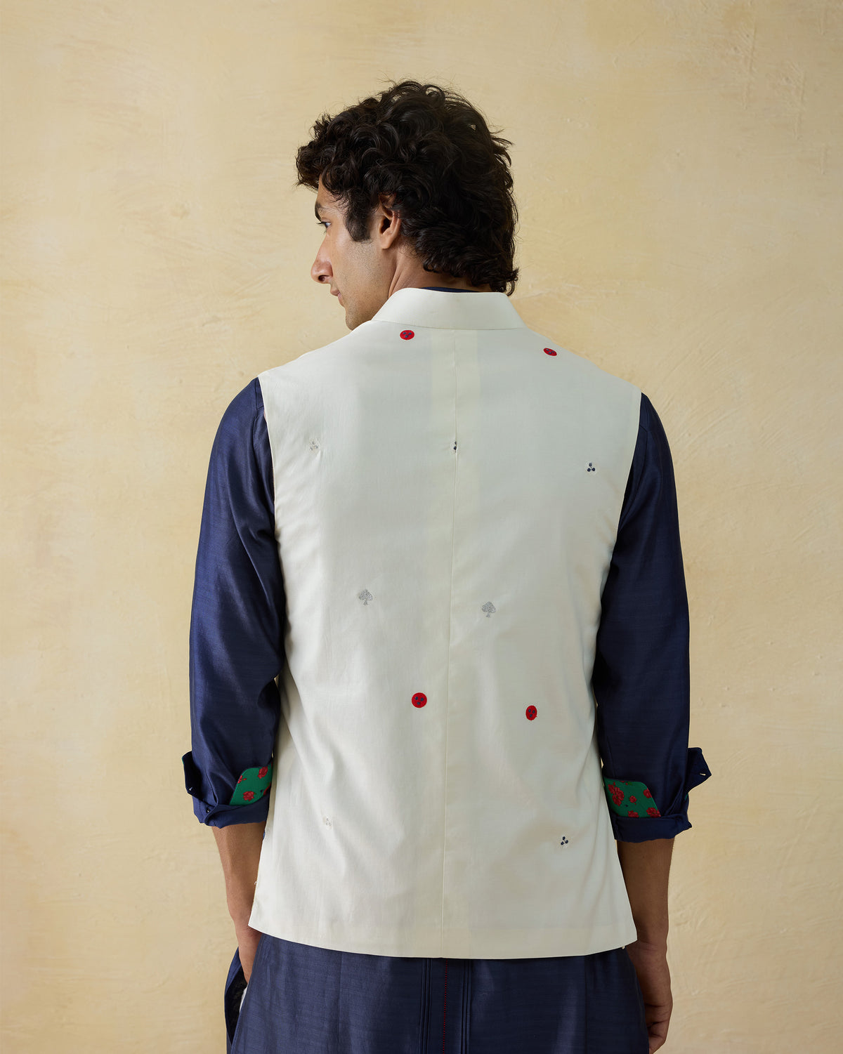 Back of an ivory Nehru Jacket with red embroidered dots over a navy shirt.