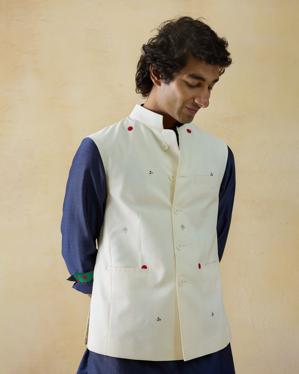 Person wearing an ivory Nehru Jacket with red embroidered dots and waist pockets.