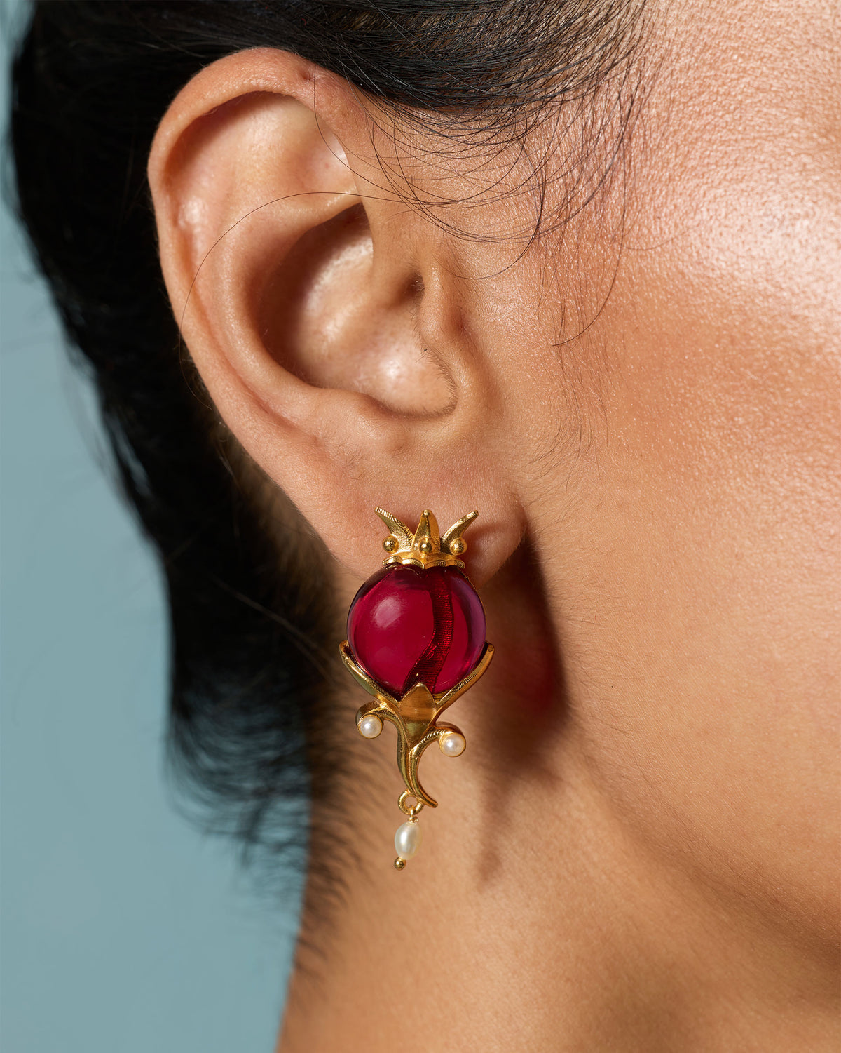 Close-up of Pom Pearl Drops worn on an ear, showing a red stone and pearl drop.
