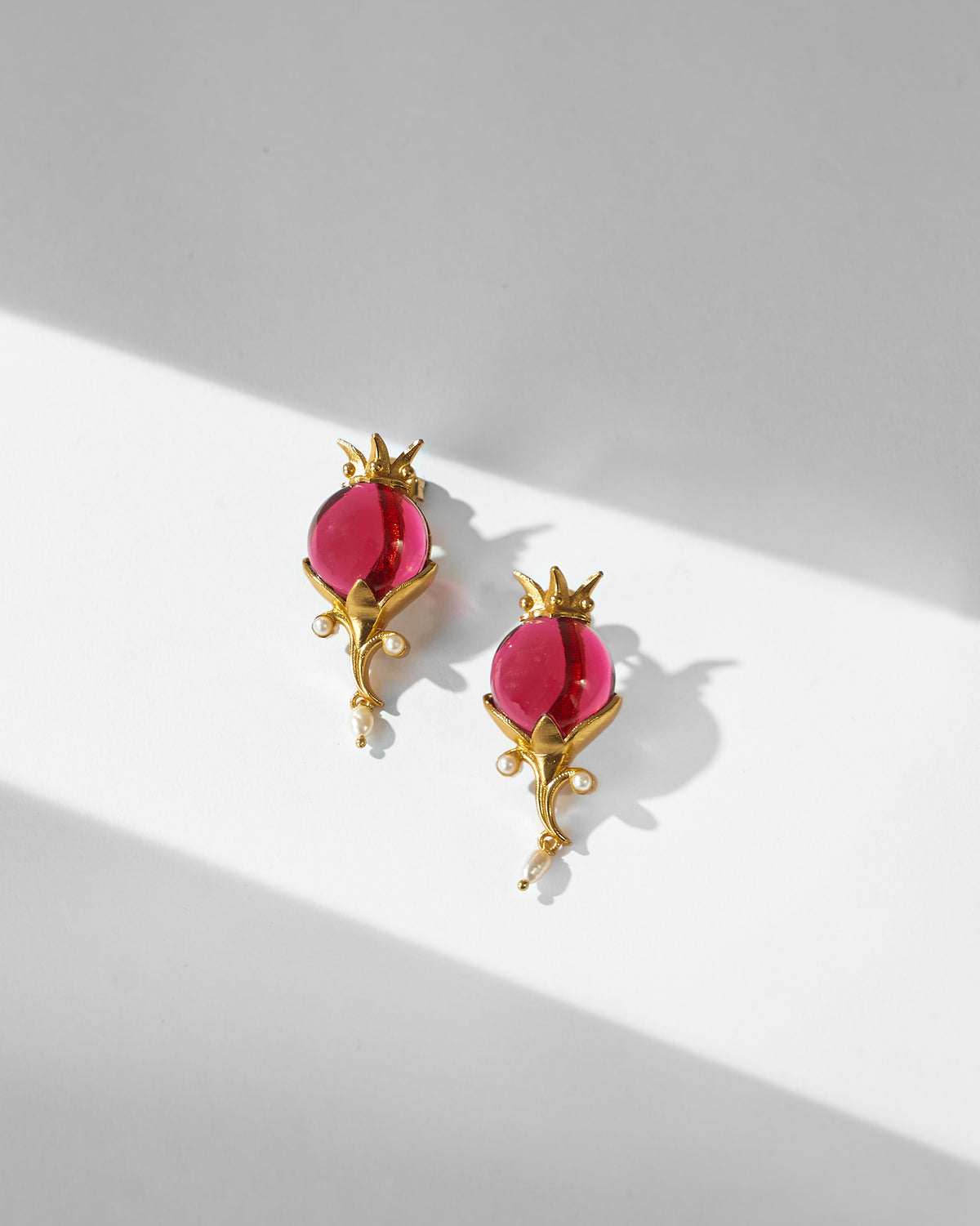 Pair of gold Pom Pearl Drops with red stones and pearl drops laid flat.