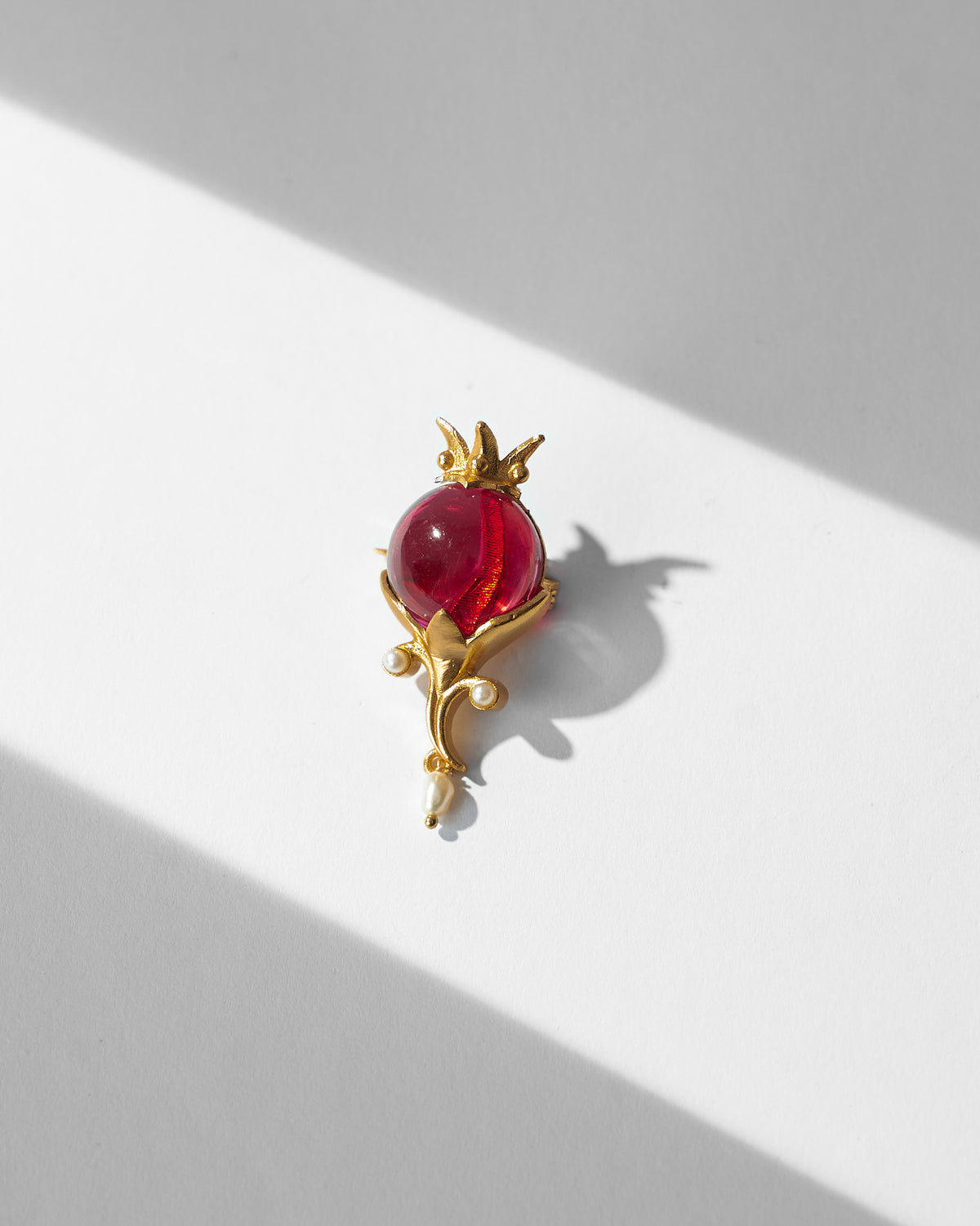 Pom Pearl Brooch laid flat with a red stone and pearl drops.