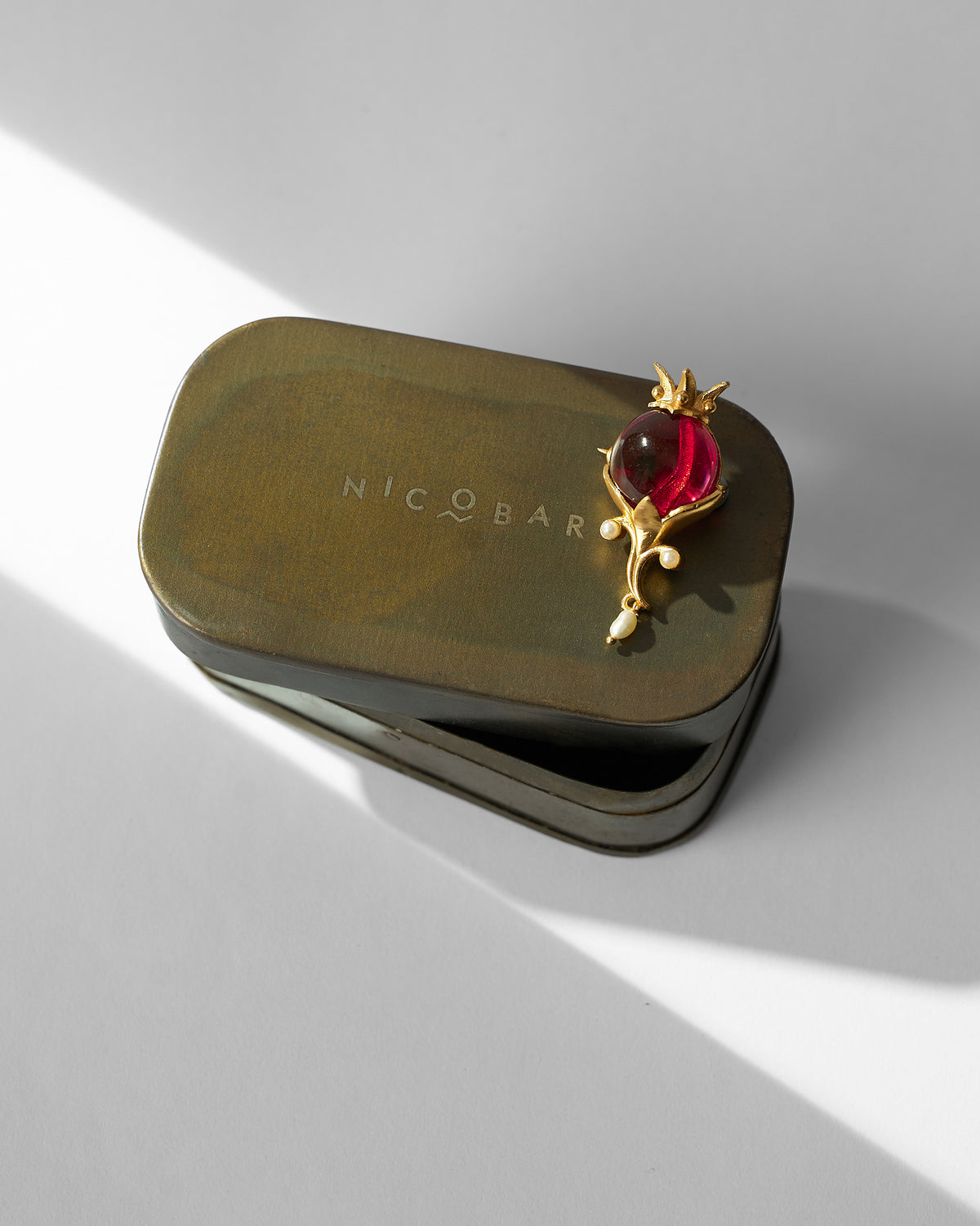 Pom Pearl Brooch with a red stone resting on a Nicobar tin.