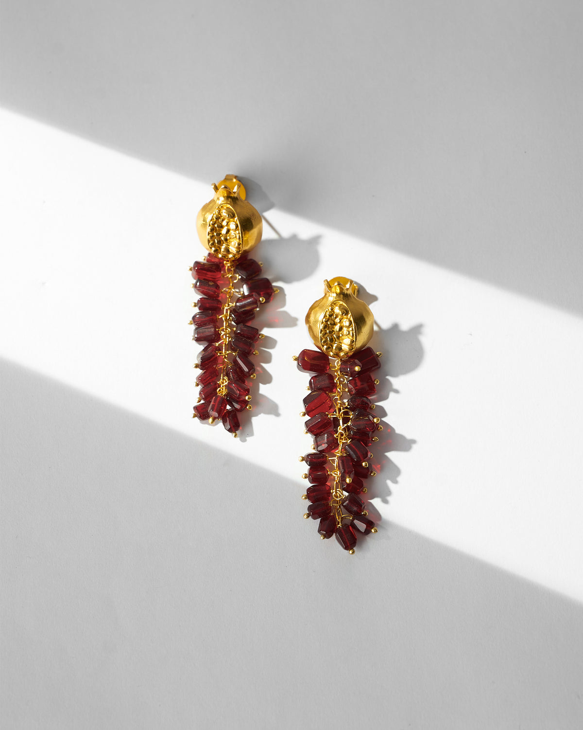 Pair of Anaar Bagicha Earring laid flat, with gold pomegranate tops and red drops.