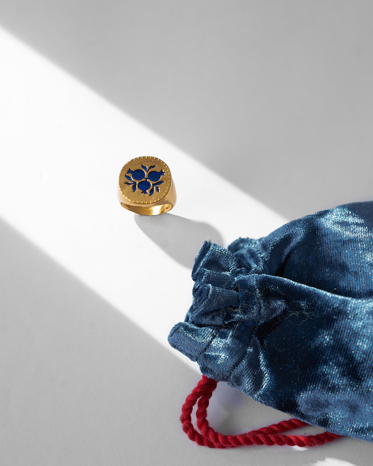 Gold Anar ring with blue enamel beside a blue velvet pouch.