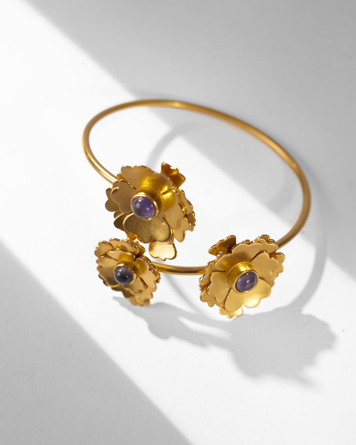 Close-up of a Kesar Phool Cuff with three gold flowers, each with a purple stone centre.