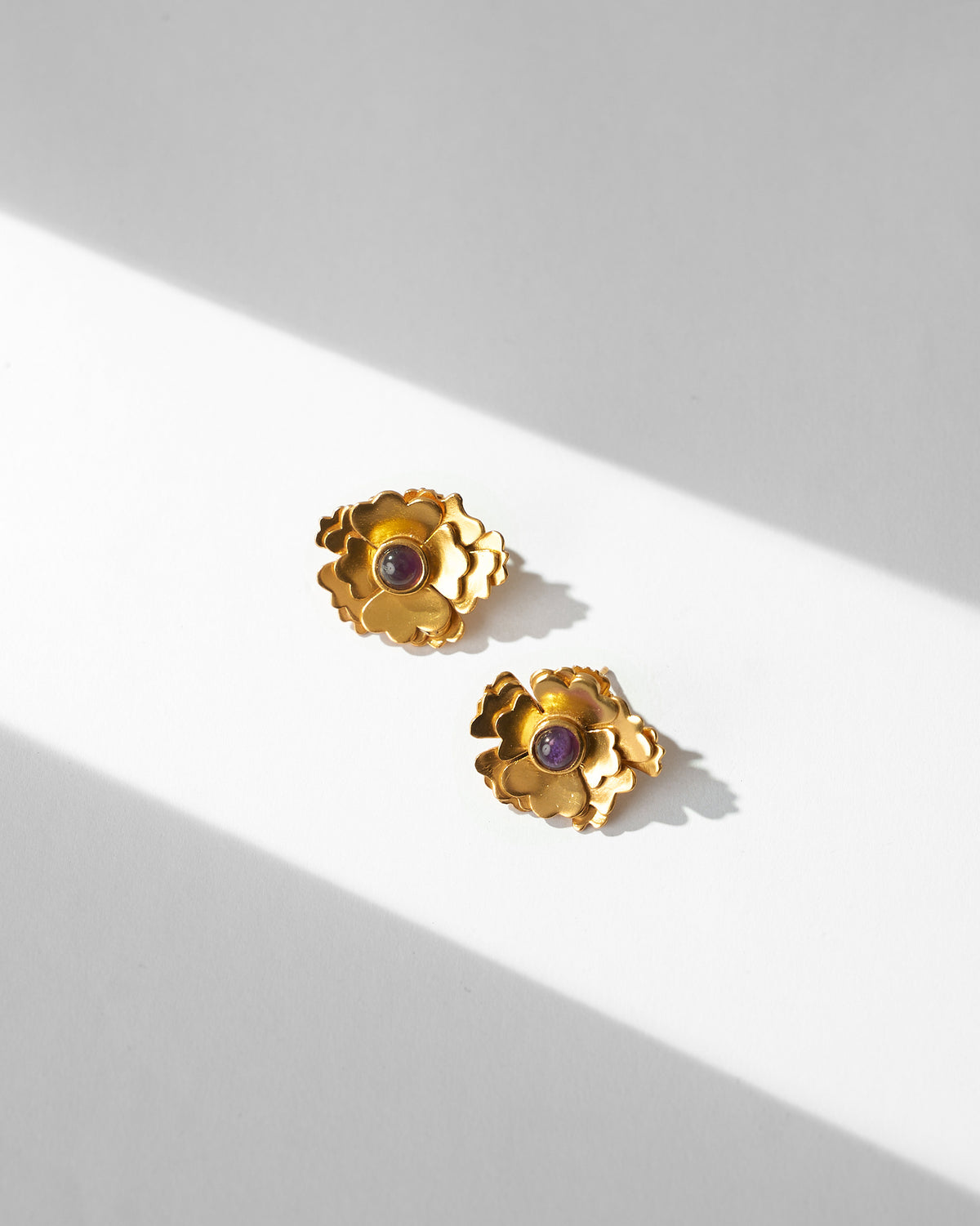 Pair of Kesar Phool Studs with purple stone centres, laid flat on a white surface.