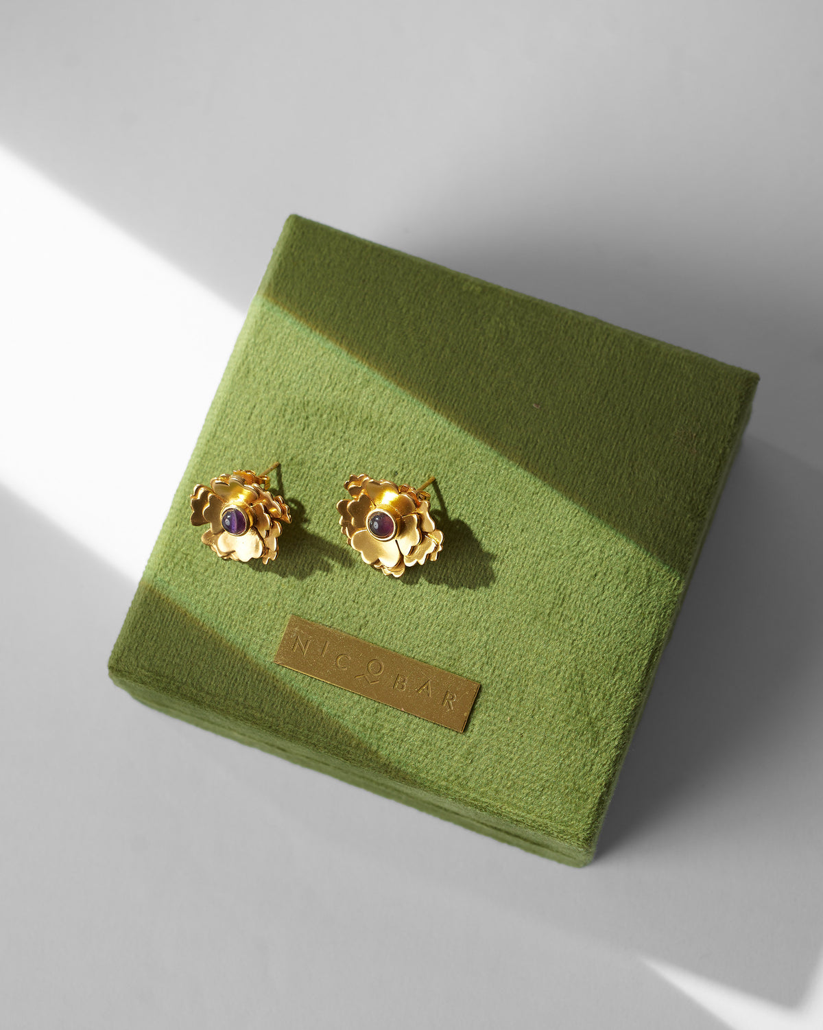 Pair of Kesar Phool Studs resting on a green velvet box.