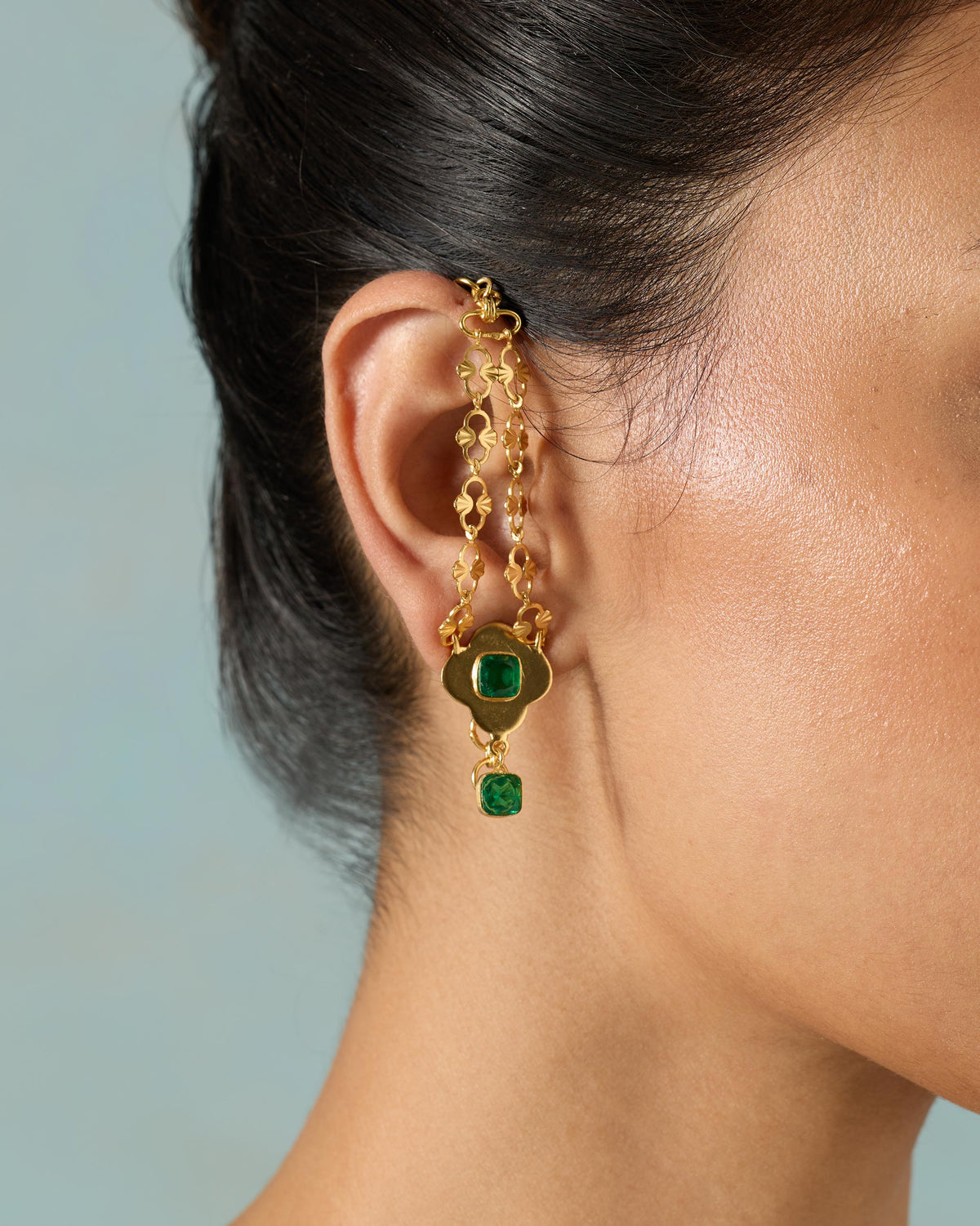 Side profile of a gold Clover Kanauti earring with green stones on a person.