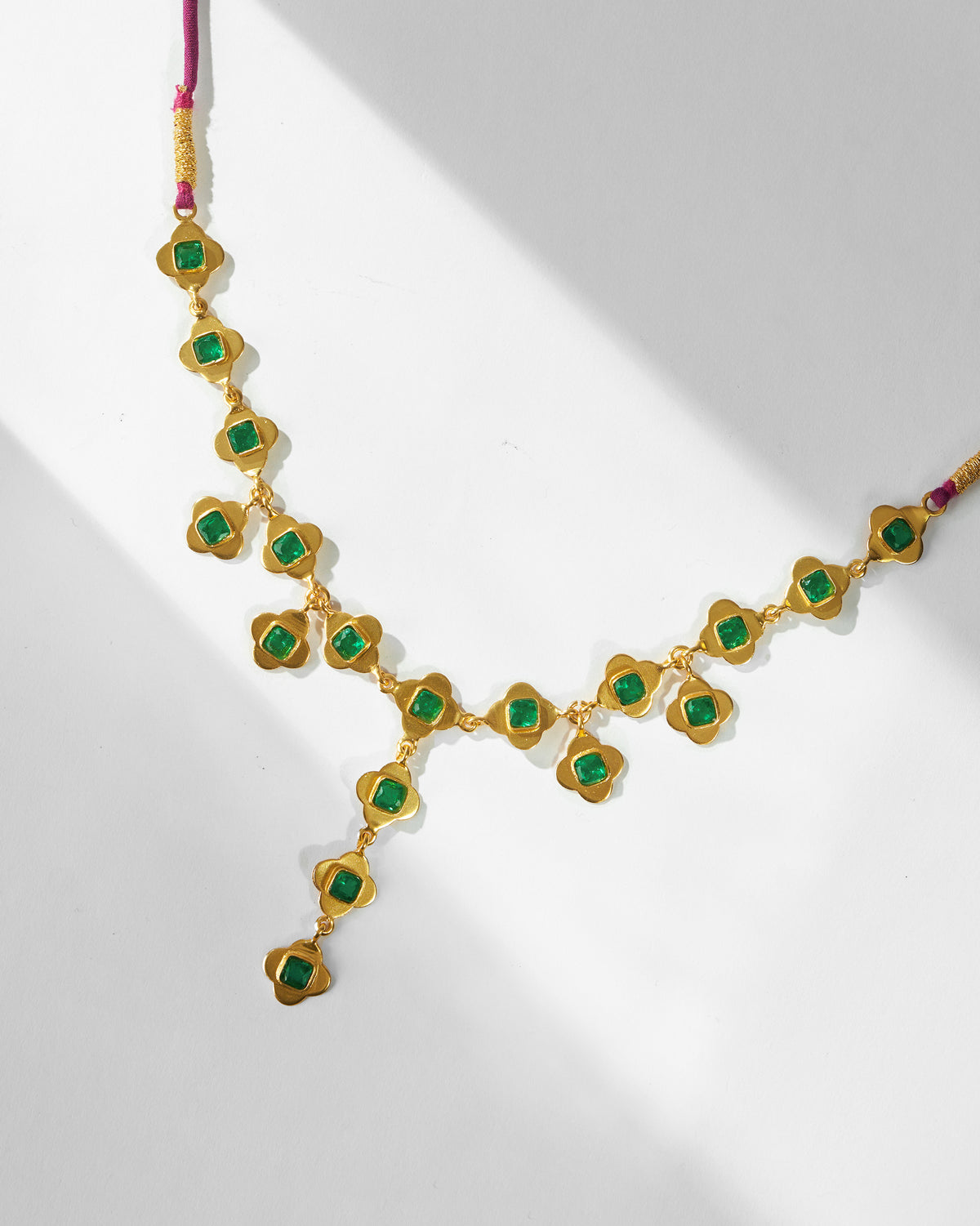 Gold Clover necklace showing linked quatrefoils with green stones.