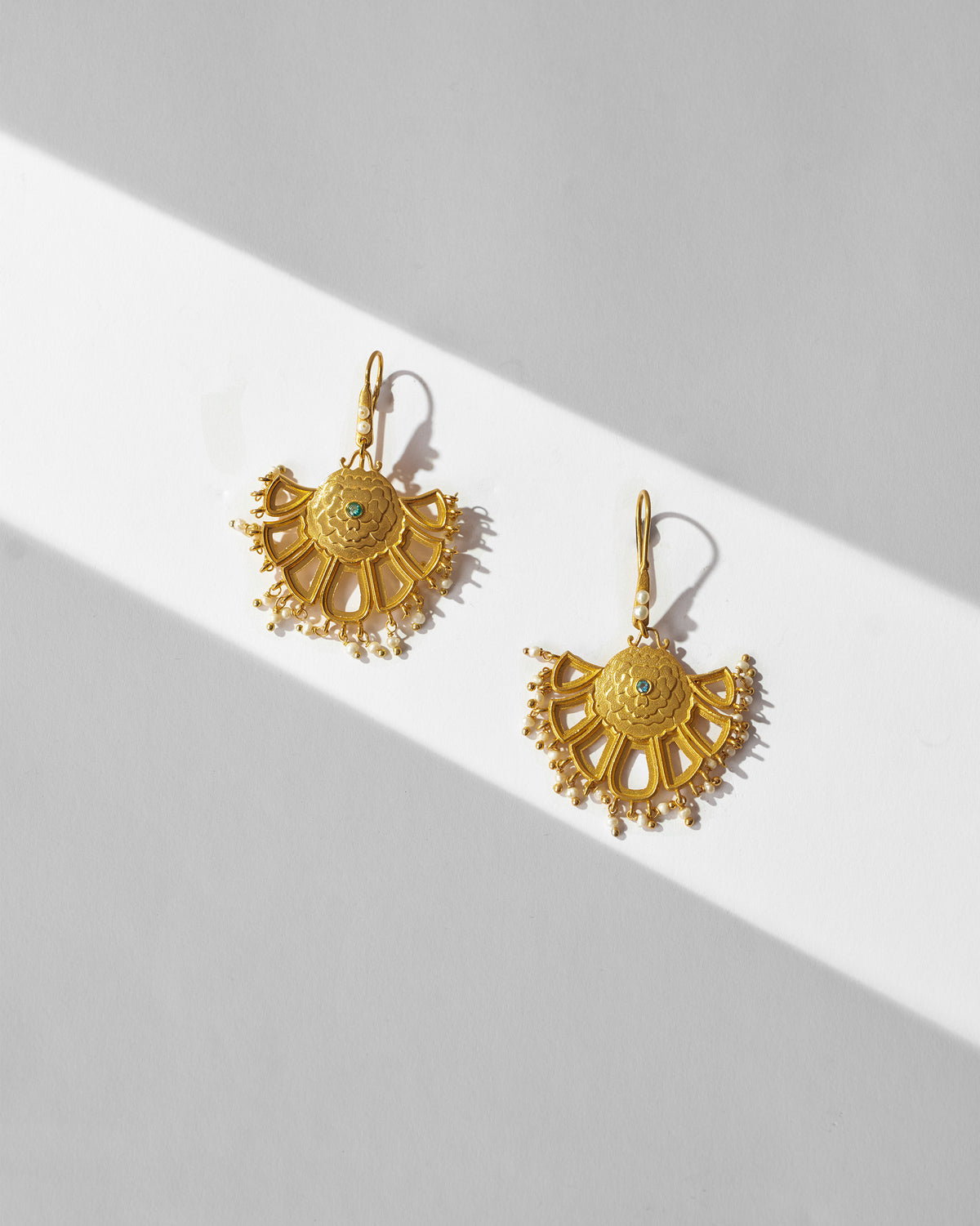 Pair of gold Marigold Earrings laid flat, showing green centre stones.