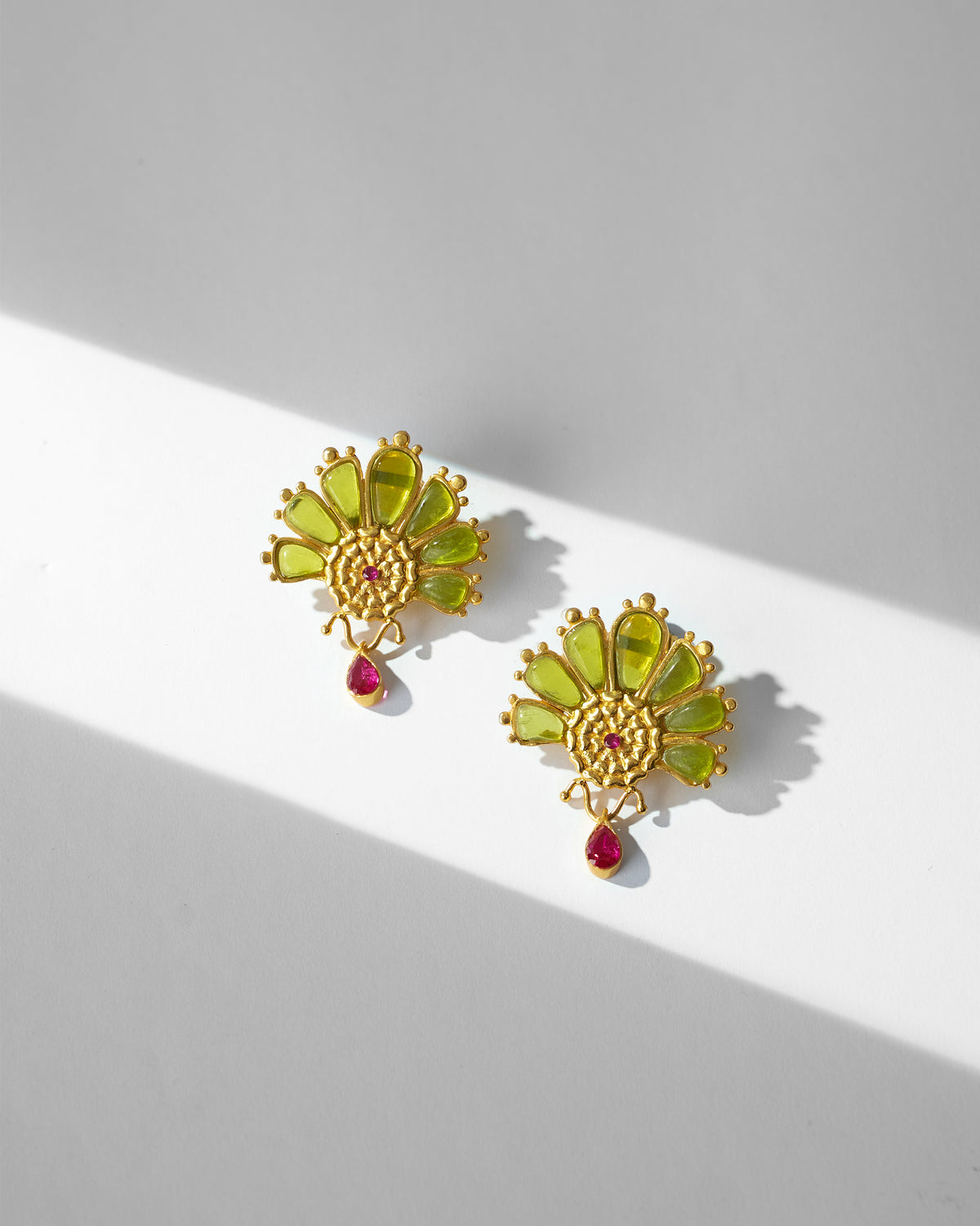 Pair of Mari-Palm earrings with green petals and pink drops, laid flat.