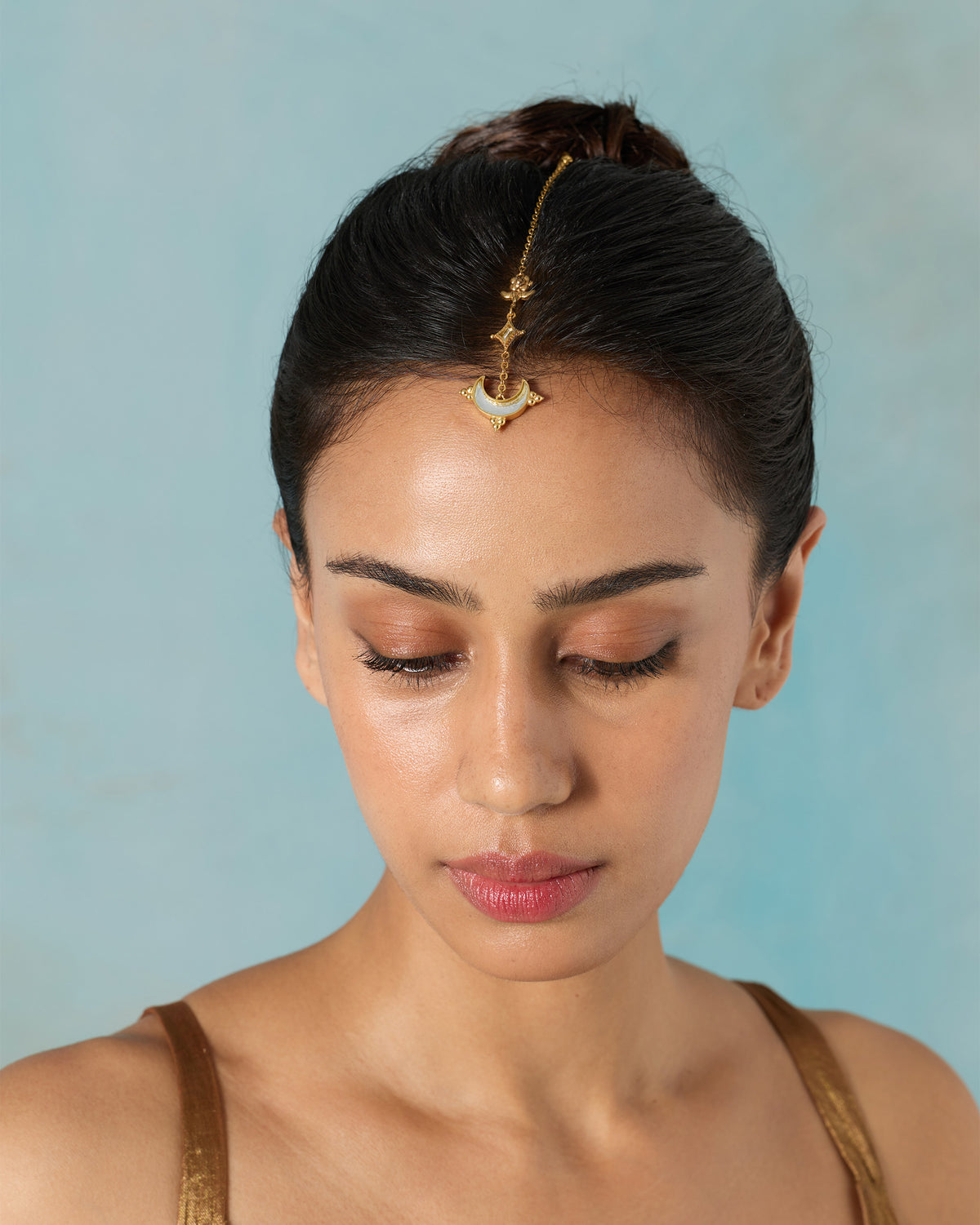Person wearing a gold Chand maangtika with a crescent mirror on the forehead.