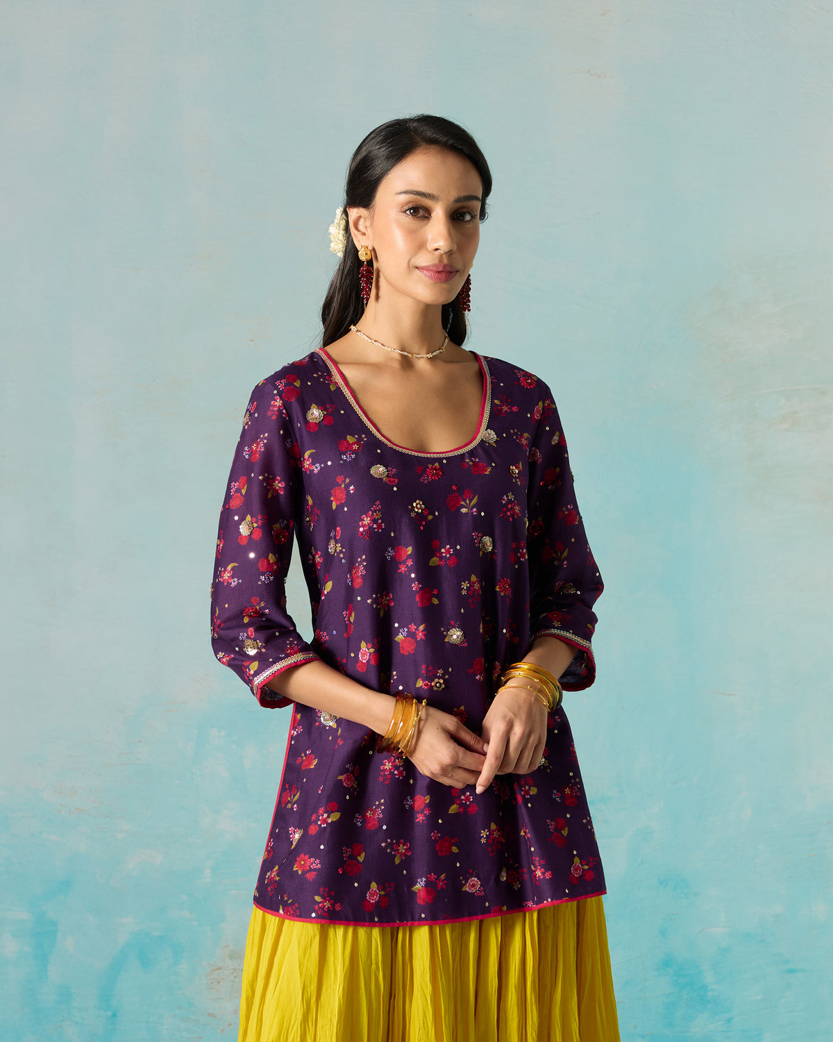 Person with hands at the waist, wearing a purple Sehra kurti with pink piping.
