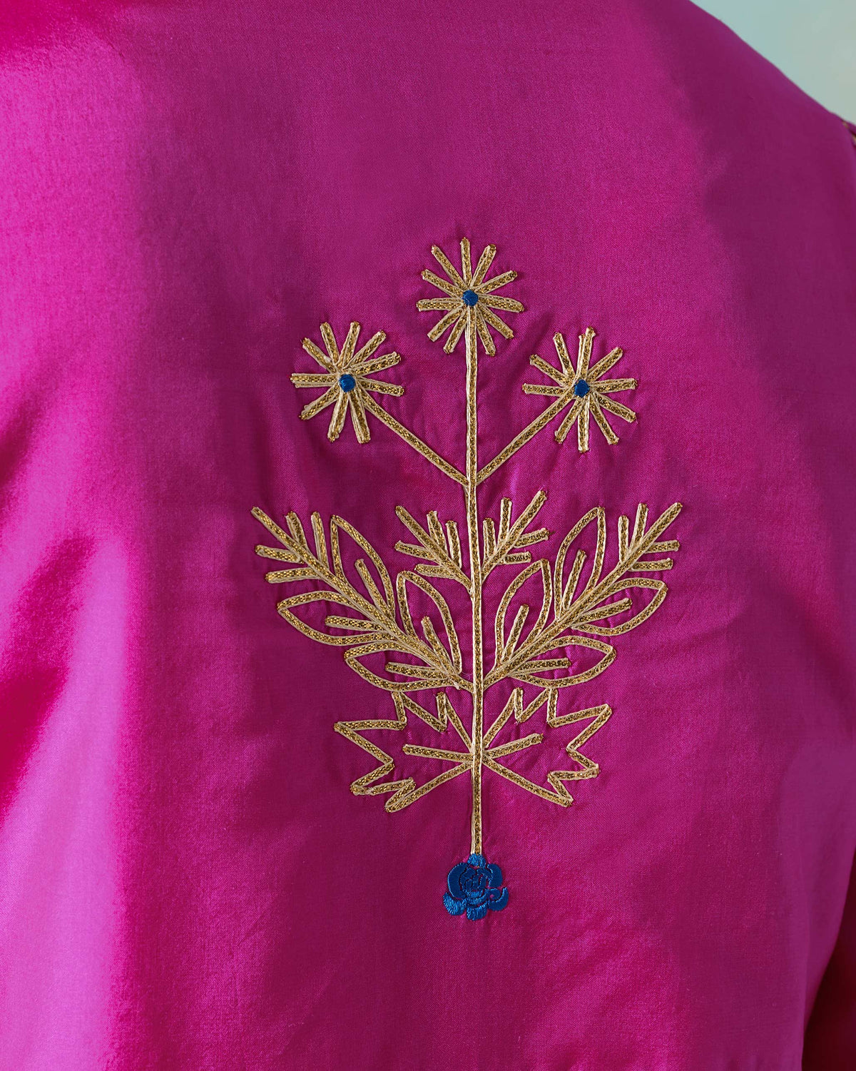 Close-up of gold thread embroidery with a blue flower on a magenta Milni kurta.