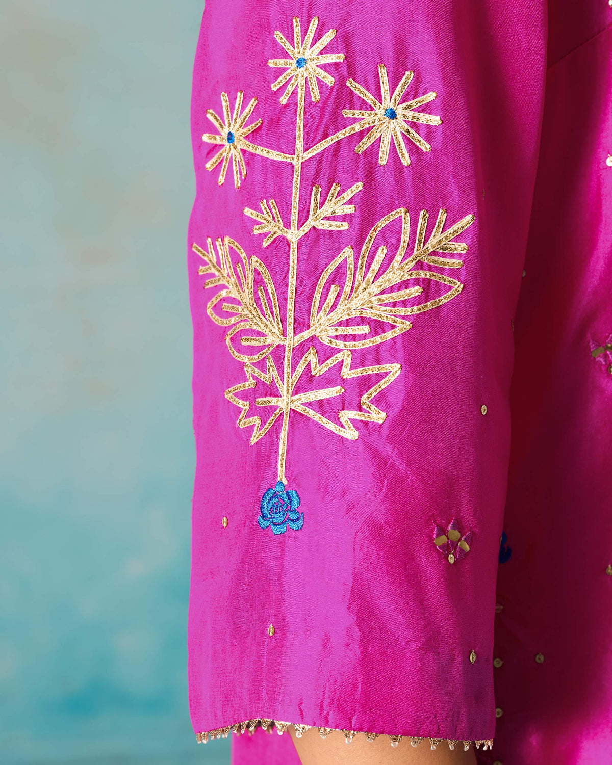 Close-up of gold embroidery on the sleeve of a magenta Milni kurta.
