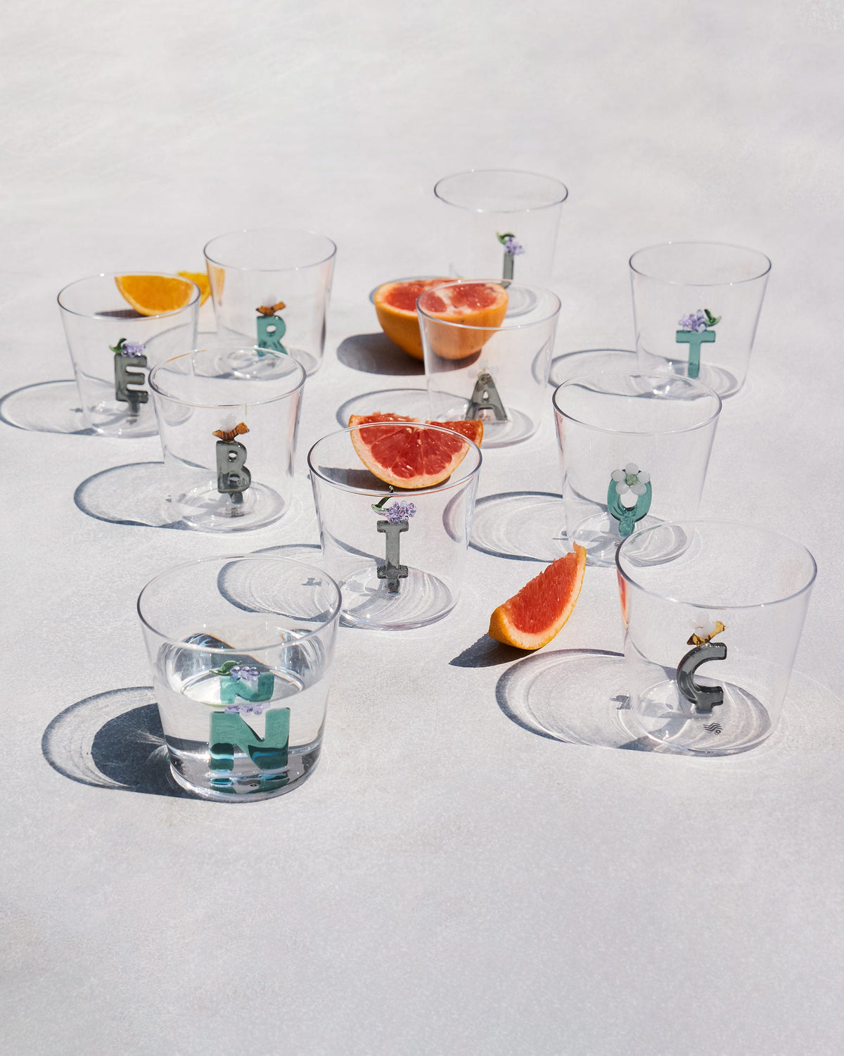 Clear Alphabet glasses with coloured letter inserts arranged with citrus slices.