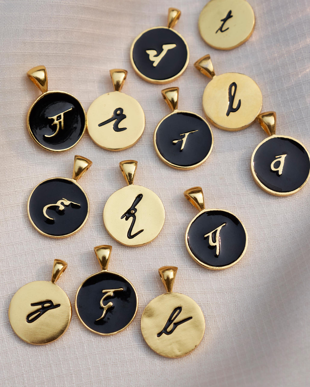 Alphabet charms in gold and black enamel scattered on linen.
