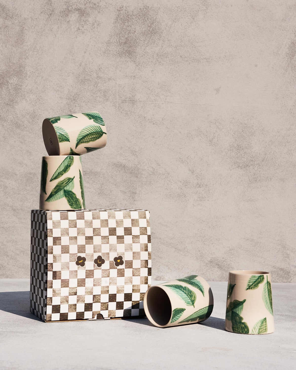 Galle kulhars with banana leaf print beside a checkered gift box.