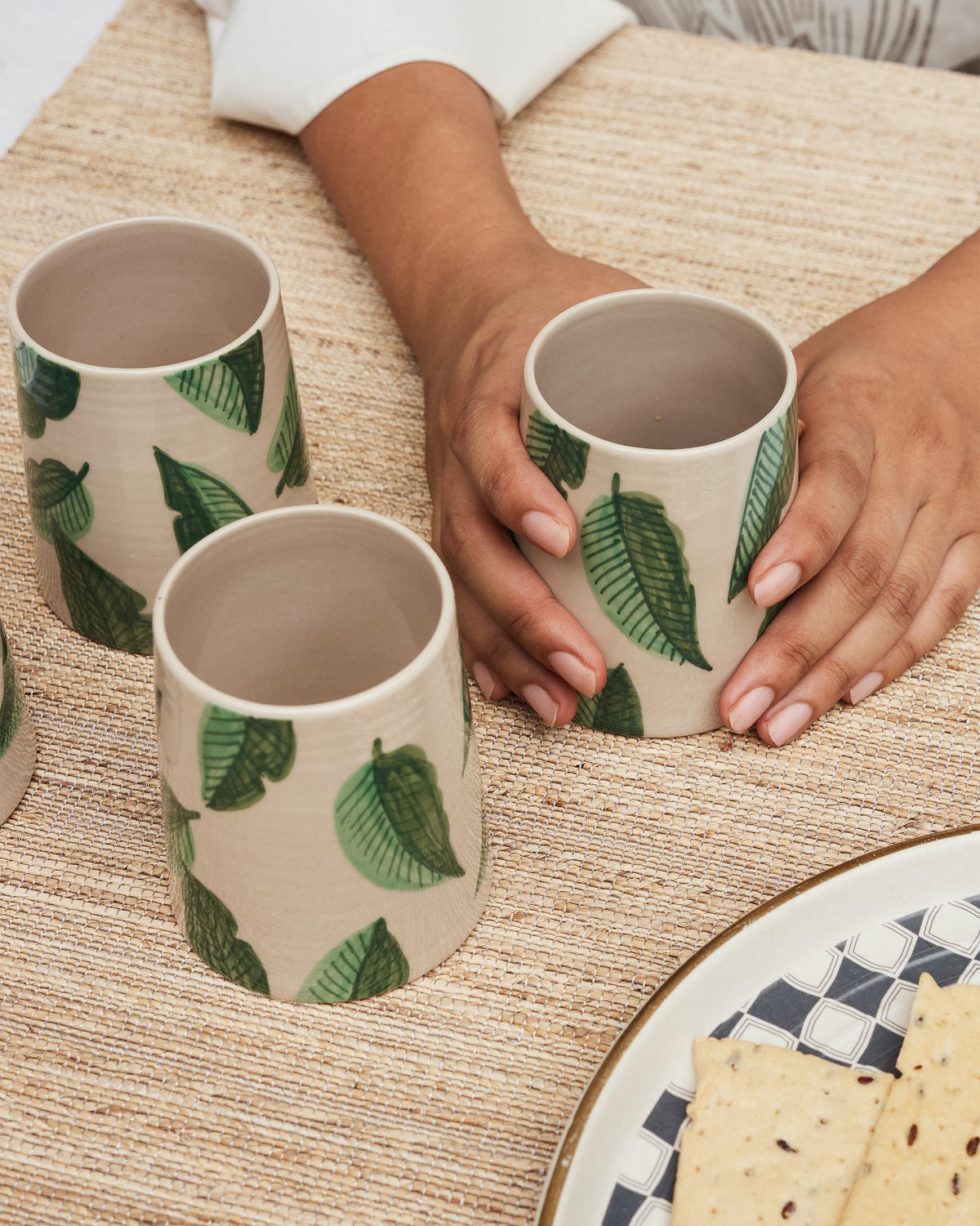 Hands holding a cream Galle kulhar with green banana leaves.