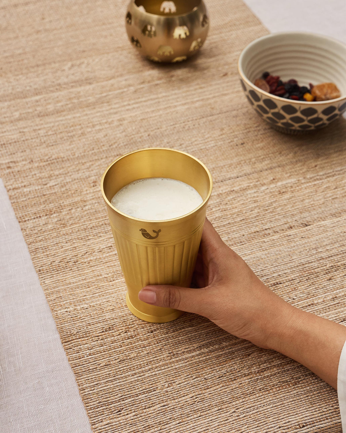 Brass Dariya lassi glass filled with a frothy drink held in a hand.