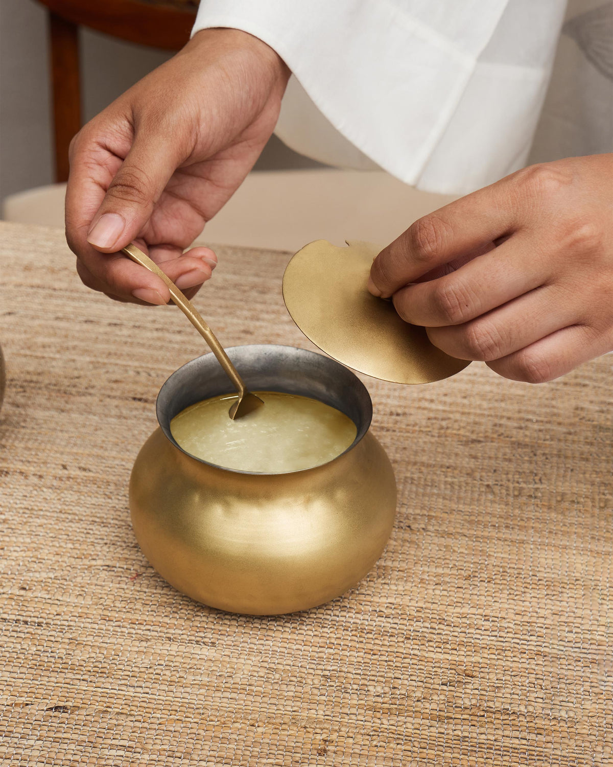 Brass Madhu ghee pot open with a ladle scooping ghee.