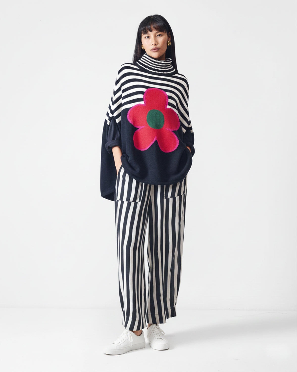 Full-length person wearing a black Rosie Sweater with a red flower on the front.