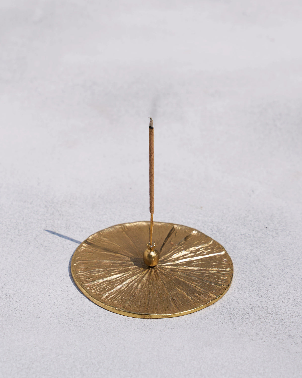 Gold Anar incense holder with a lit stick standing in the centre.