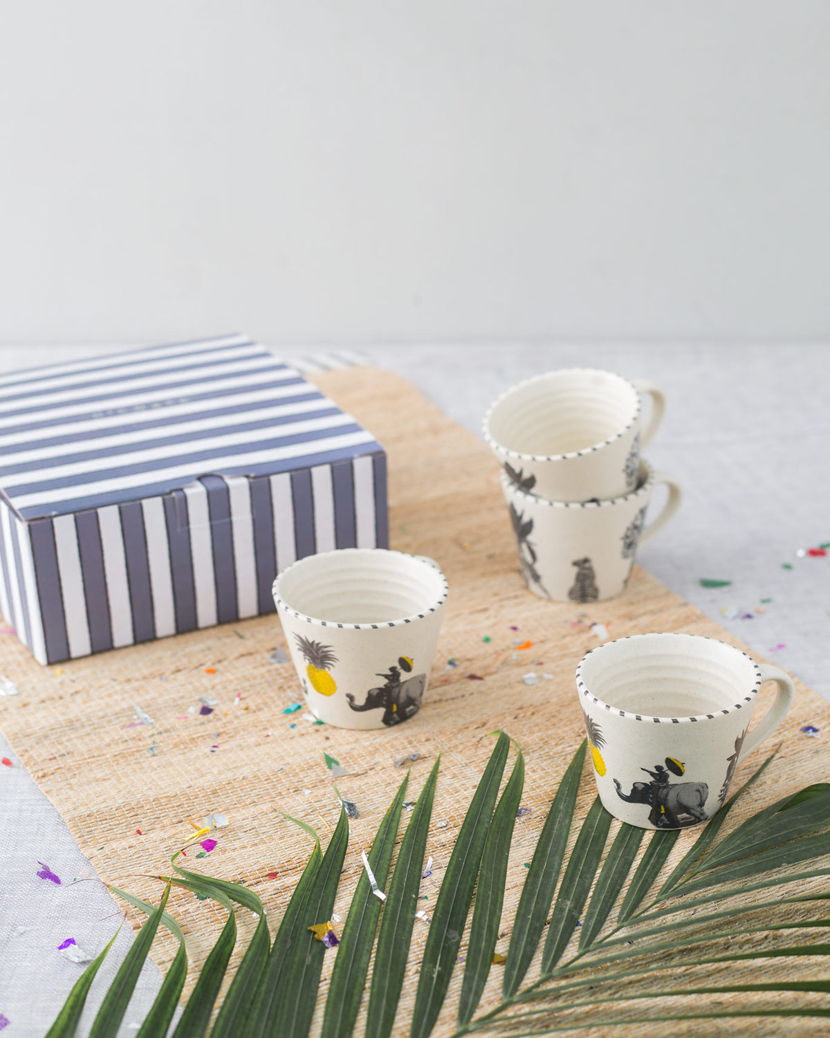 Four Haathi Sher Espresso Mugs on a woven mat beside a striped gift box.