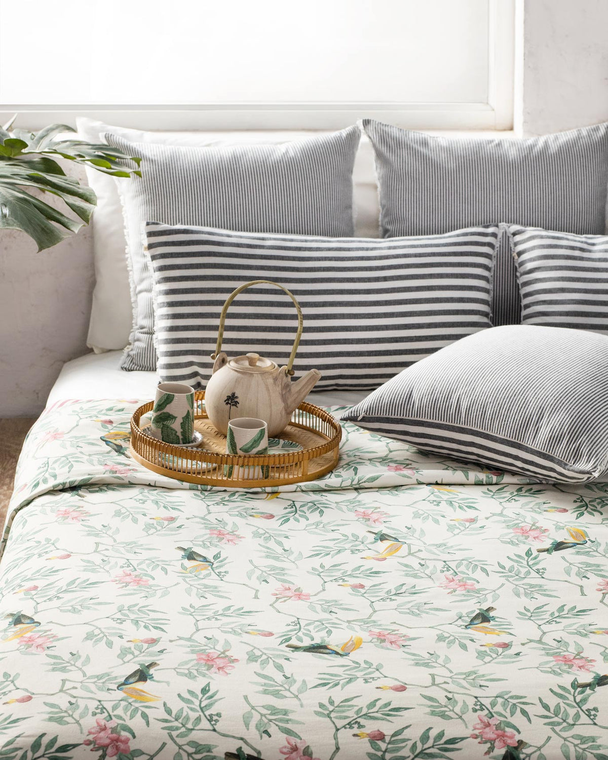 Ivory Nakano bed cover with bird and leaf print styled on a bed with striped pillows.