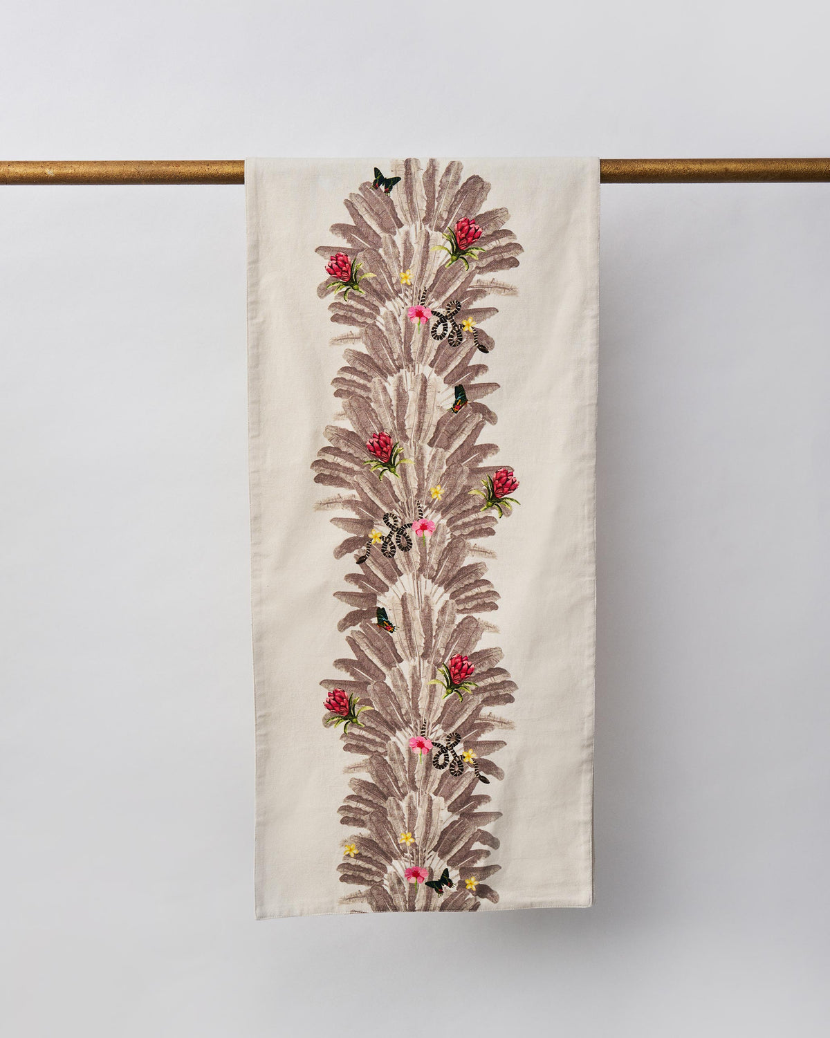 Ravenala Runner hanging on a brass rod, with grey palm fronds and red and pink flowers.
