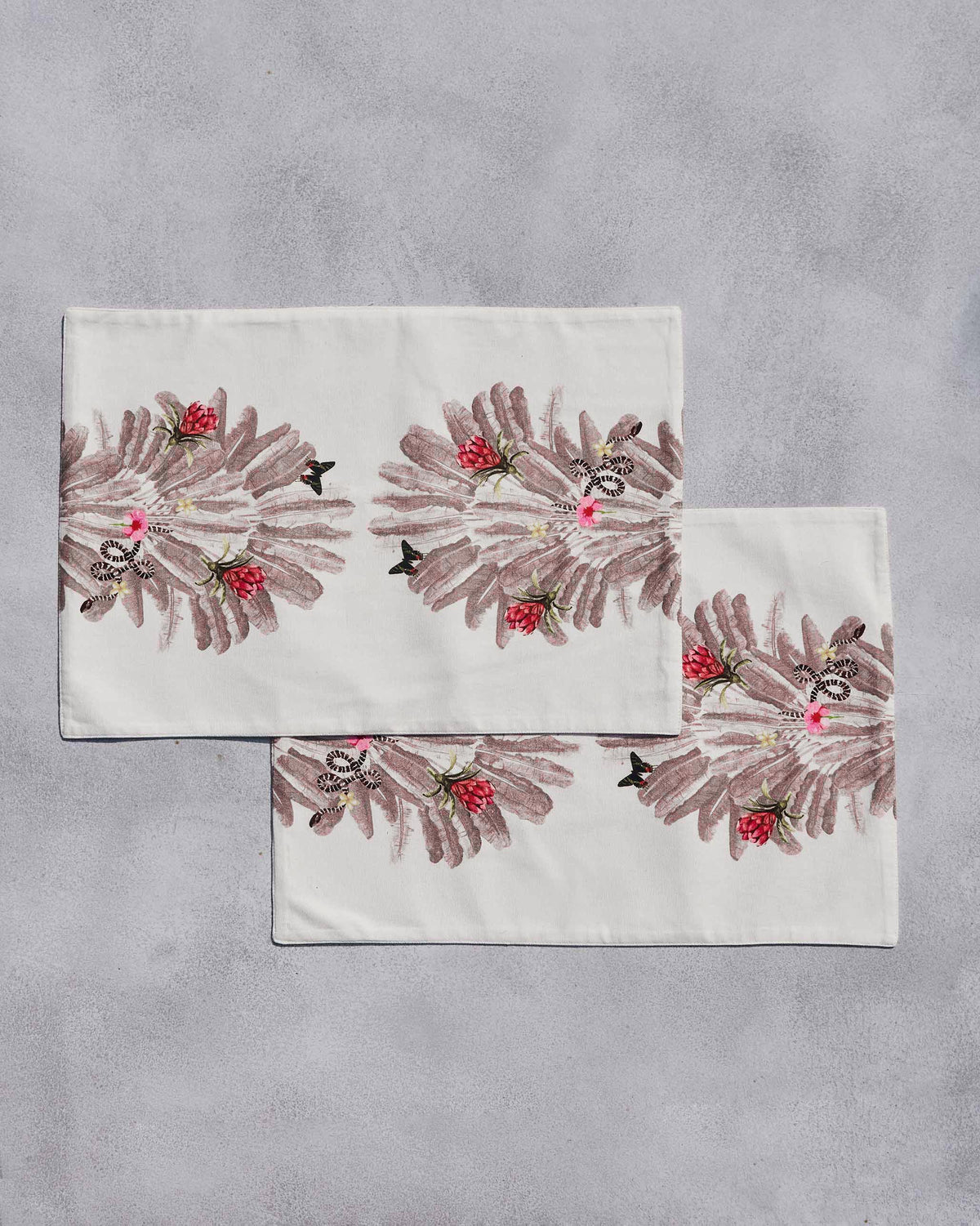 Pair of Ravenala Placemats laid flat with a red flower and leaf print.