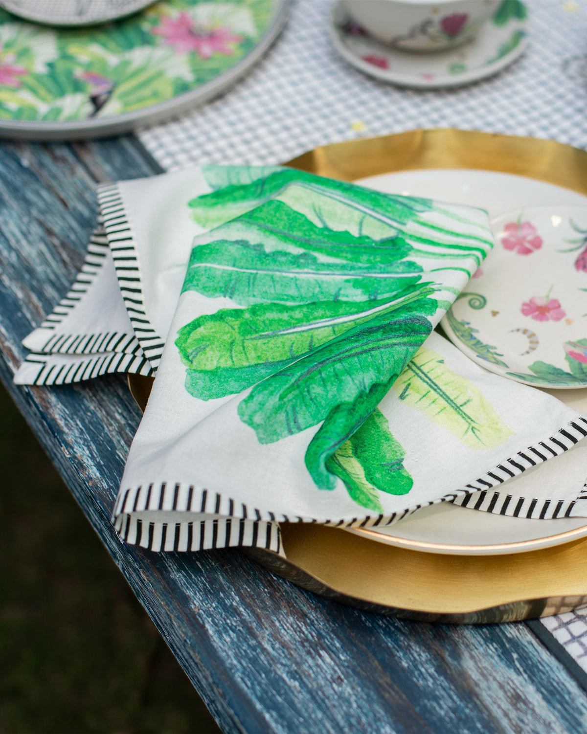 Ravenala dinner napkin with green leaves draped on a place setting.